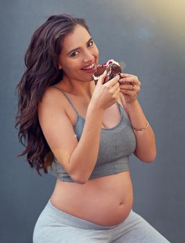 Im sorry for what I said when I was hungry. a pregnant woman eating a slice of cake against a gray background.