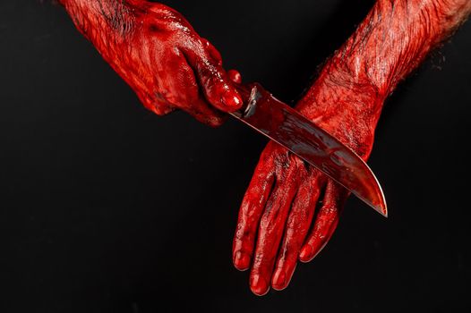 A man wipes a bloody knife with his hand on a black background.
