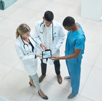 Group of doctors working on digital tablet while standing in the hospital hallway and talking. Top view of healthcare employees analyzing test results and treatment in medicare clinic with technology