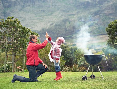 Barbecue bonding. a father giving his son a high five while theyre having a barbecue outside.