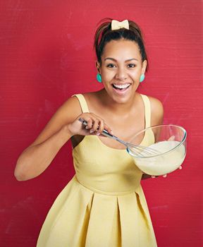 I only bake from scratch. Studio shot of a young woman mixing batter in a bowl against a red background.