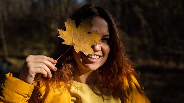 Red-haired Caucasian woman holding a fallen maple leaf. Autumn Walk.