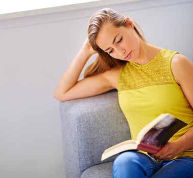 Theres no enjoyment like reading. a young woman reading a book on her sofa at home.