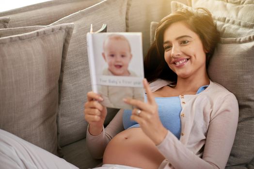 Reading a best seller baby book. a young pregnant woman reading a baby book at home.