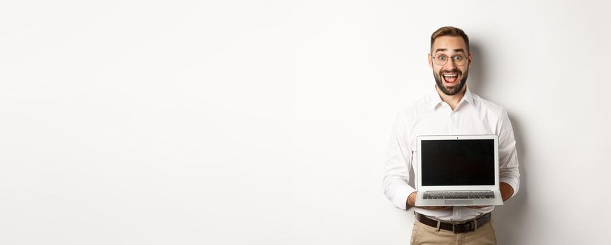 Excited businessman showing something on laptop screen, standing happy over white background