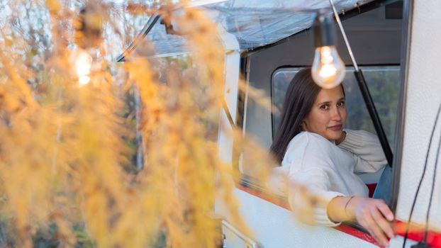 Portrait of a caucasian woman looking out of a trailer window. Travel in a camper in autumn.