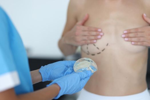 Doctor draws marks on female breast before cosmetic surgery operation and holds silicone implant
