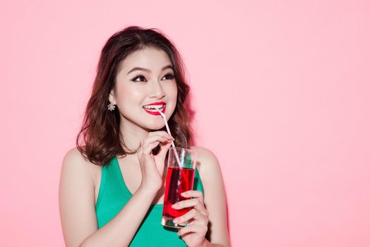Beautiful girl drinking a cocktail against pink background.