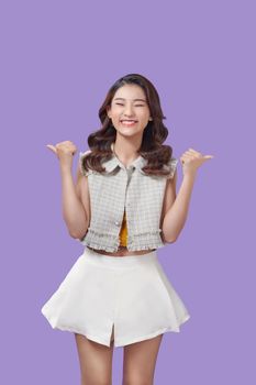Showing and Pointing Two Product With Thumbs Of Beautiful Asian Woman Isolated On purple Background