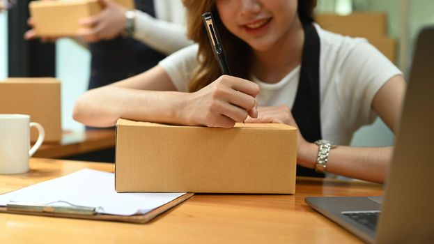Smiling woman preparing parcel boxes of product for delivery and writing address on cardboard box
