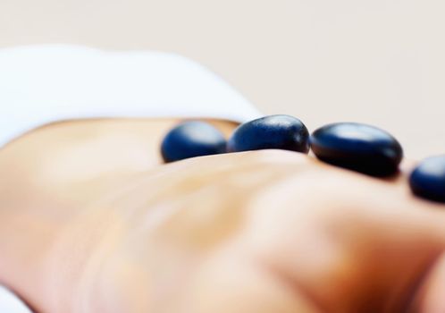 Therapy - Arrangement of hot stones placed on a womans back. Closeup of a woman getting a hot stone massage at a day spa.