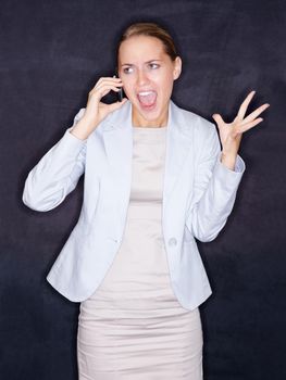 Angry business woman screaming over mobile phone against black. Angry young business woman screaming over the cellphone against black background.