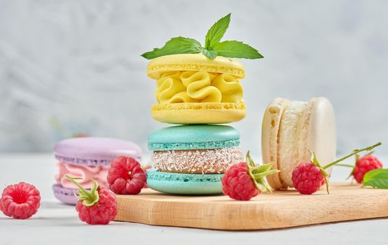 A stack of multicolored macaroons and red raspberries on a white background. 