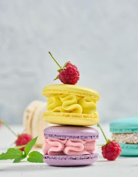 A stack of multicolored macaroons and red raspberries on a white background.