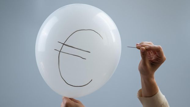 A woman bursts with a needle a balloon with the inscription euro.