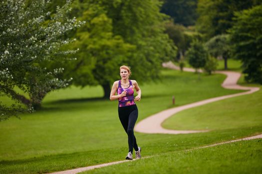 She loves a solitary jog. a woman jogging along a foothpath in a park.