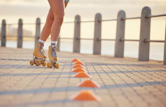 Woman roller skating with fitness cones outdoor on the promenade at the beach during summer. Girl practicing her skating skill while training for a sports activity in nature at the ocean.