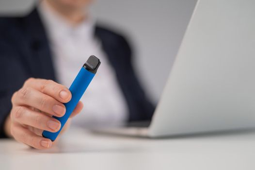 Business woman holding disposable vape while sitting at laptop.