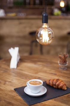 Fresh roasted coffee in a white coffee cup with tasty croissant on a vintage pub