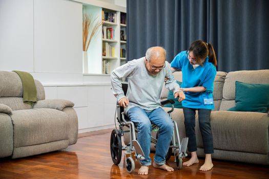 Asian nurse assisting helping senior man patient get up from wheelchair for practice walking