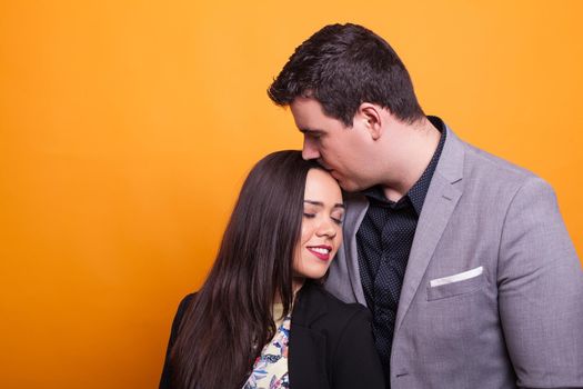 Young husband showing his affection to her wife over yellow background