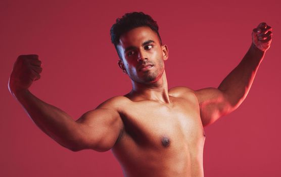 Bodybuilder, muscle and fitness with a nude man model posing shirtless in studio with a red background. Naked, strong weightlifter with a healthy male flexing arms inside for health and wellness