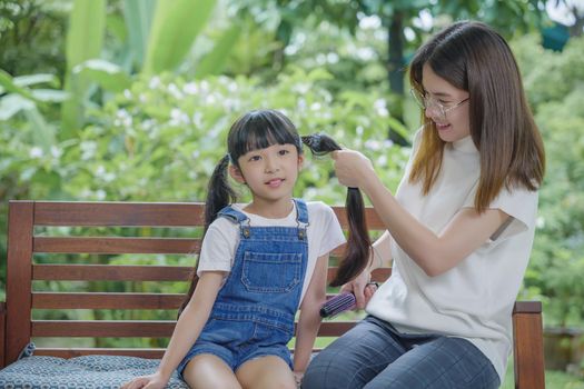 Happy family beautiful mother woman brushing her daughter hair while sitting outdoor at home