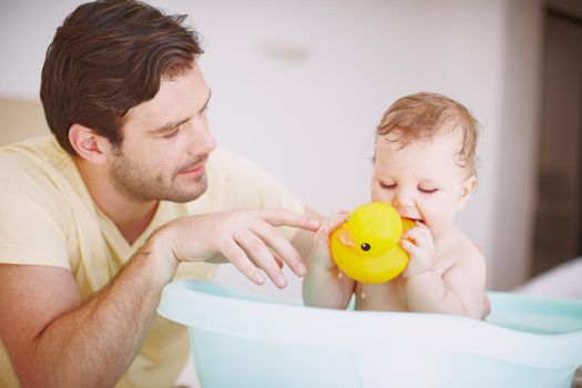 Bathtime with Dad and Mr Duck. A young father looking at his daughter with fondness while shes playing in the bath.