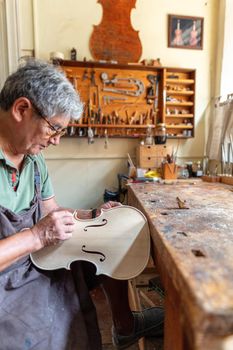 luthier carving the shape of the outside of the front of a violin with gouge