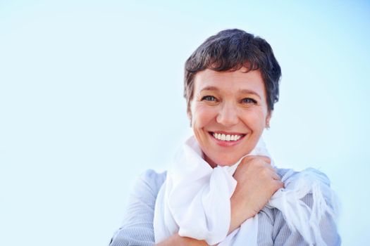 Woman enjoying outdoors. Closeup of beautiful mature woman smiling against sky with scarf around her neck.