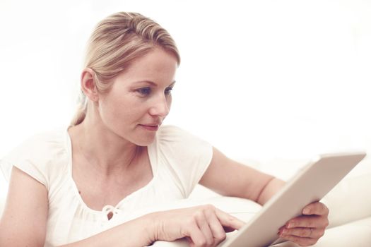 Selecting something good to read - eReaders. An attractive blonde woman using a tablet while sitting at home.