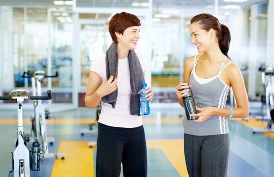Female friends at the gym. Two fitness women in workout clothes talking and smiling at gym.