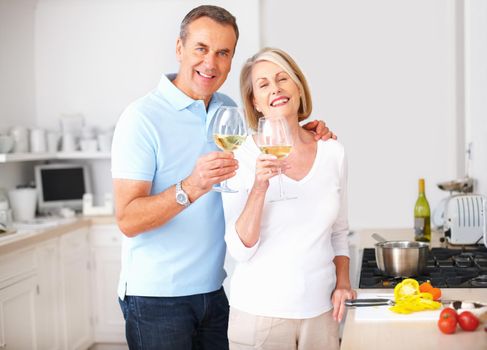 Cheerful senior couple toasting wine glasses at kitchen. Portrait of a cheerful senior couple toasting wine glasses at kitchen.