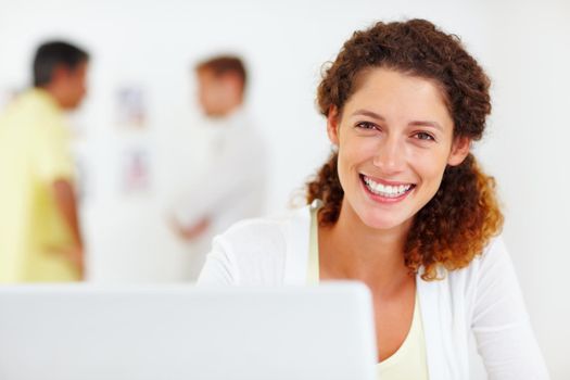 Attractive business woman using laptop. Closeup portrait of attractive business woman using laptop with colleagues in blurred background.