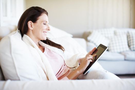Reading a romance novel on her e-reader. An attractive woman using a digital tablet while sitting on a sofa.