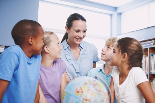 Teach us more about the world. A pretty young geography teacher teaching her students about the world using a globe of earth.