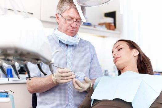 Dentist holding false teeth in clinic. Portrait of dentist holding false teeth with female patient in clinic.