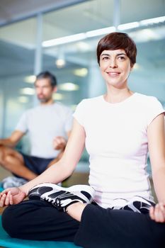 Lotus position. Full length of a beautiful woman in lotus position with man in background.