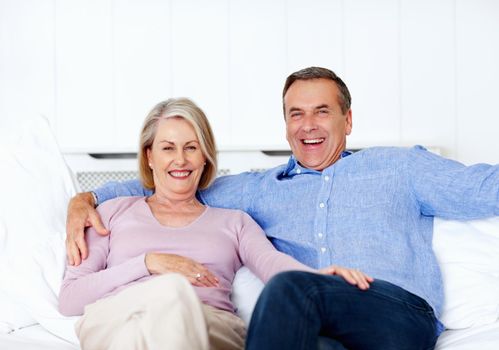 Cheerful mature man and wife sitting on sofa at home. Portrait of a cheerful mature man and wife sitting on sofa at home.