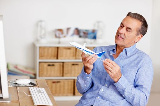 An elderly man looking at toy plane with computer on desk. Planning vacation - An elderly man looking at toy plane with computer on desk.