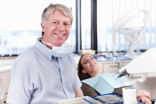 Happy dentist with patient. Portrait of mature dentist smiling with female patient in background