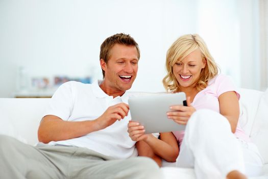 Cute couple using tablet pc. Cute couple sitting on sofa using tablet pc and smiling.