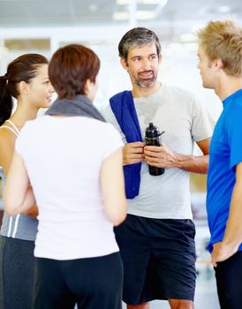 Friends relaxing after exercise. Portrait of mature man talking with friends at fitness center.