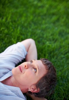 Woman relaxing on grass. Thoughtful mature woman relaxing while lying on grass.
