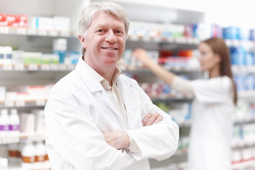 Pharmacist with female assistant. Portrait of handsome pharmacist with female assistant in background.