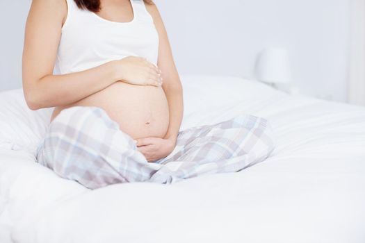 Holding her future. Cropped image of a young woman holding her pregnant belly on her bed.