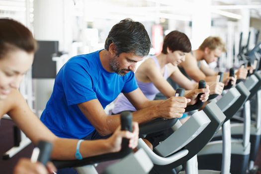 Its important to warm up properly. a row of people working out on the exercise bikes at the gym.