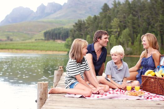 Family fun in the fresh air. Happy young family enjoying a lakeside picnic from a jetty.