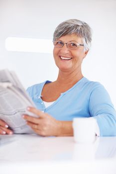 Newspaper with morning cup. Smiling mature woman reading newspaper while enjoying morning cup of coffee.
