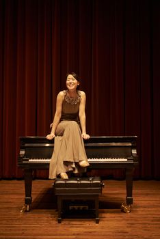 Shes a professional piano player. a young woman sitting on her piano at the end of a musical concert.